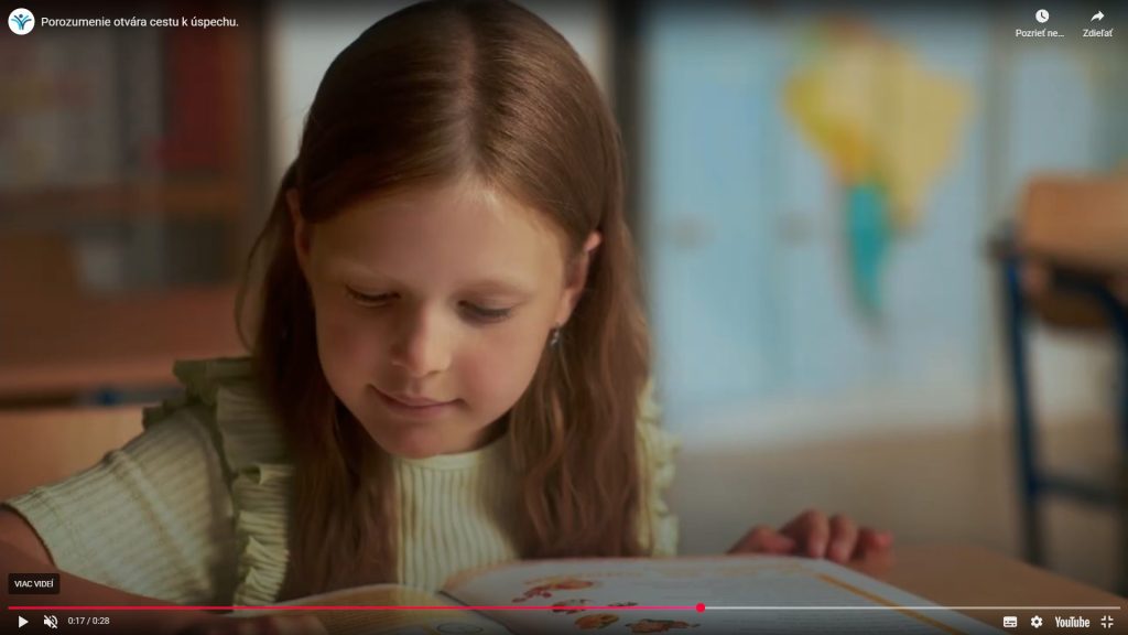 Na fotografií sedí dievča za školskou lavicou, číta knihu a číta z nej