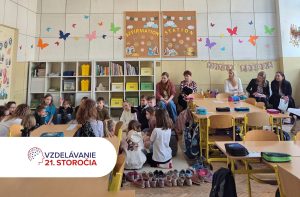 Na fotografii je školská triede, kde sedia vzadu na stoličkách učitelia a učiteľky z iných škôl počas EDUKAfestu 2026 a pozerajú sa na deti a pani učiteľku, ktorá vedie otvorenú hodinu a spolu s deťmi sedí na koberci.