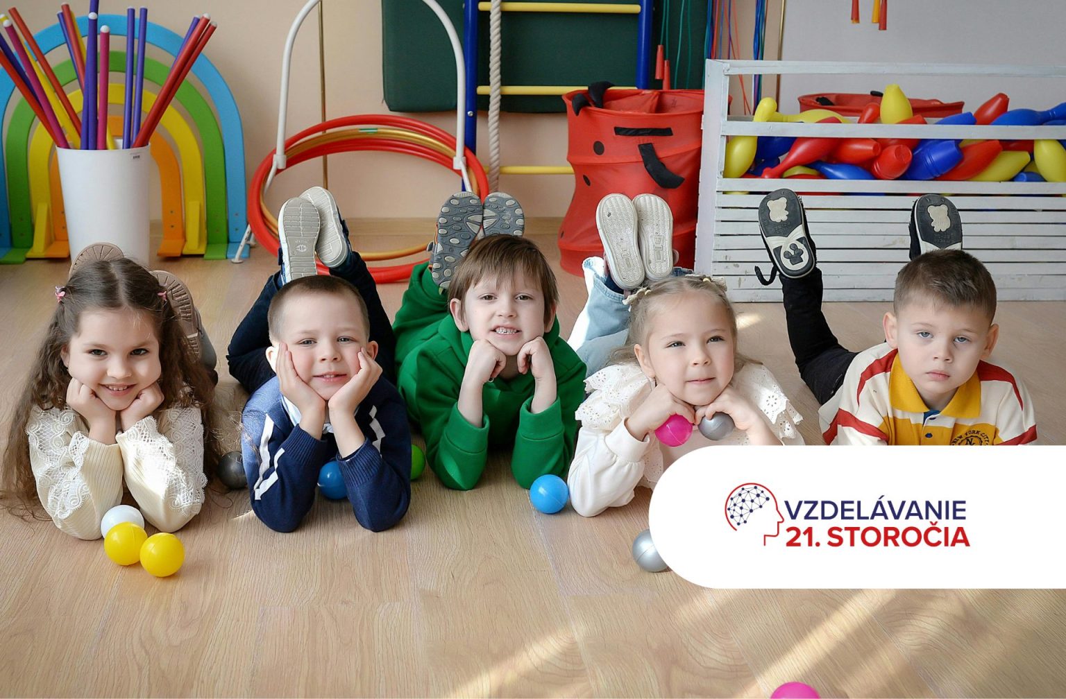 Päť detí pozerá do objektívu a leží na zemi v školskej triede a podopiera si hlavu rukami.